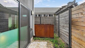 A modern outdoor space with a wooden fence, a metal bench, and a glass door leading to a building. - Ember & Glow Loft Retreat (Seattle)