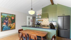 A modern kitchen with green cabinets, a stainless steel refrigerator, and a wooden dining table with chairs.
