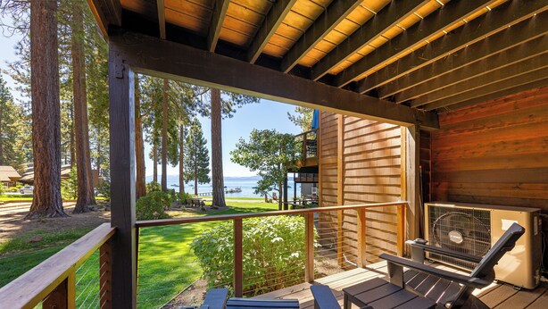 A wooden deck with a view of a lake and mountains, outdoor seating, and a covered area with a grill.