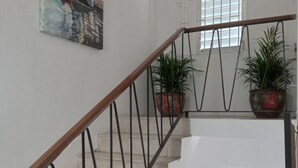 A staircase with a wooden handrail and metal balusters, flanked by potted plants and artwork. - Enjoy Beverly Hills, Kingston, Jamaica, 4 bdrms, AC, WiFi, Spacious, Quiet, Safe (Kingston)