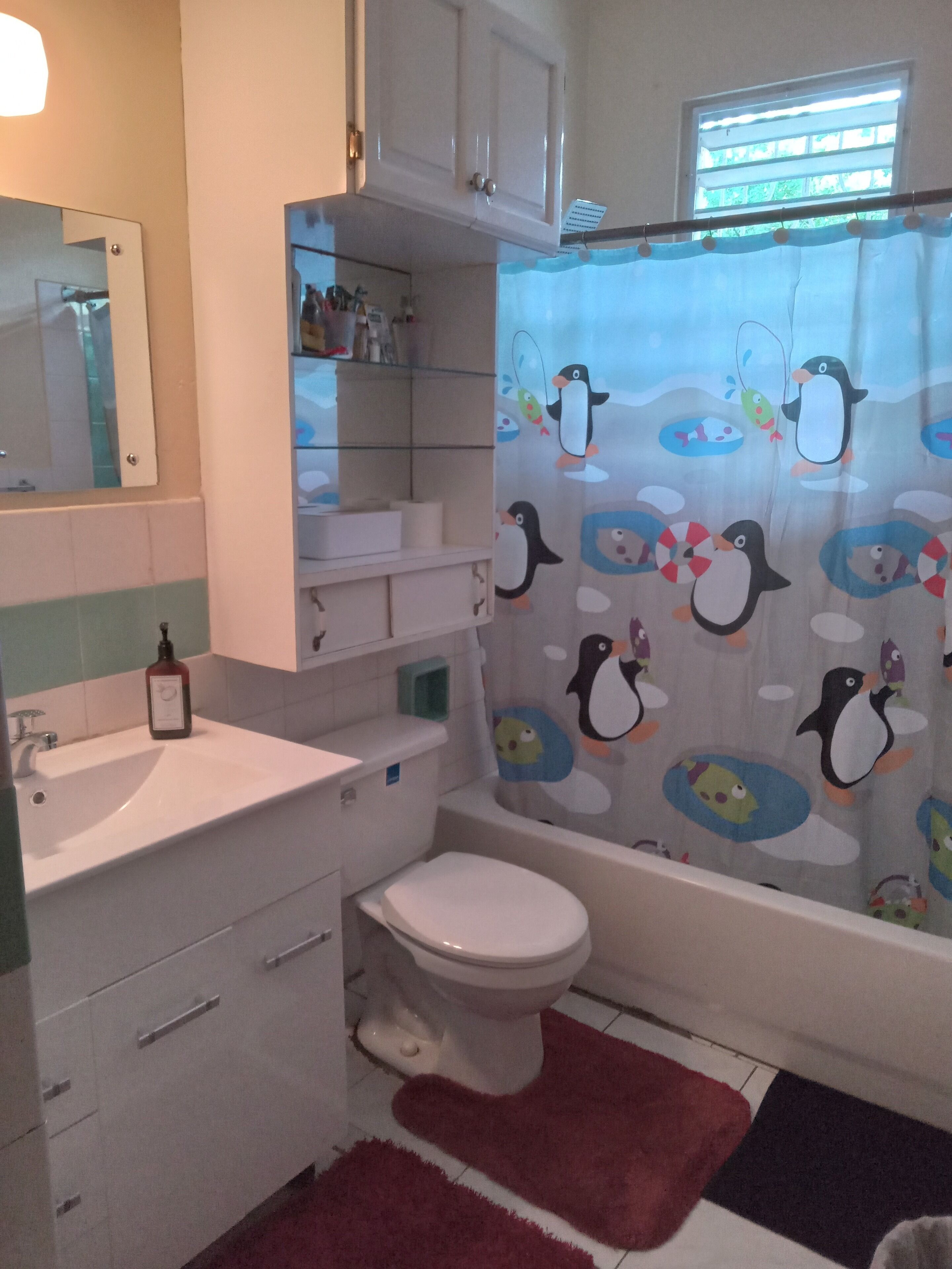 Une salle de bain équipée d’un WC, d’un lavabo et d’un meuble de rangement. On y trouve un rideau de douche orné de motifs de pingouins.