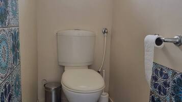 A small bathroom with a toilet, a bidet, and a trash can.
