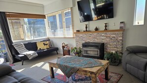 Una sala de estar con chimenea de piedra, televisor de pantalla plana, sofá, mesa de centro y un ventanal con persianas.