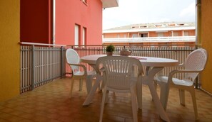 Ein Balkon mit rundem Tisch, vier Stühlen, einem Blumentopf und Blick auf ein Gebäude mit Balkonen.