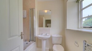 Een kleine badkamer met een badkuip, wastafel, toilet en een raam voor natuurlijk licht.