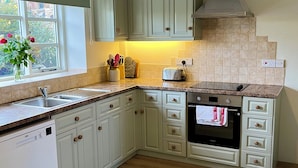 Een keuken met lichtgroene kastjes, een inbouwoven, een vaatwasser en een raam met bloemen.