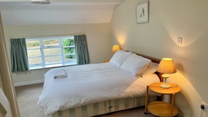Een slaapkamer met een bed, een bedlamp, een raam met gordijnen en een afbeelding aan de muur.