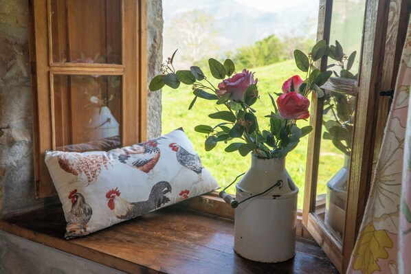 A rustic room with a wooden bench, a white vase with pink roses, and a pillow with rooster designs.