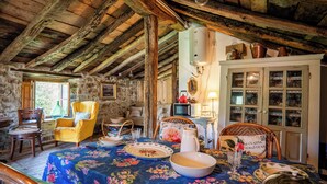 A rustic dining room with a wooden ceiling, stone walls, and a table set with floral tablecloth. - Cosy cottage in Los Valles Pasiegos, Cantabria: Lo Lucas 1920 (San Roque de Riomiera)