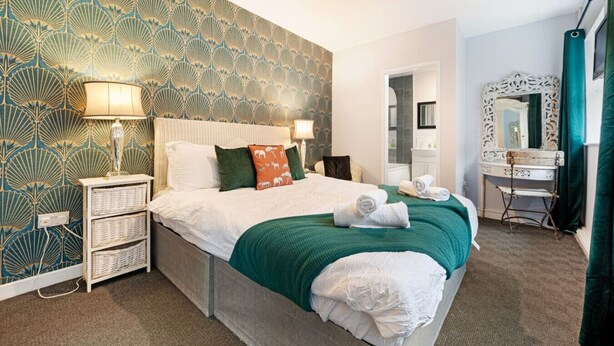 Hotelkamer met een groot bed, twee nachtkastjes, een kaptafel met spiegel en behang met een patroon.