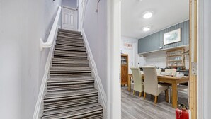 Een trap met gestreept tapijt leidt naar een eethoek met een houten tafel en stoelen.