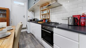 Een kleine keuken met witte kastjes, een gasfornuis, een inbouwoven en een houten eettafel met stoelen.