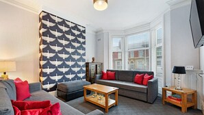 Een woonkamer met een grijze bank, een houten salontafel en een behang met een patroon.