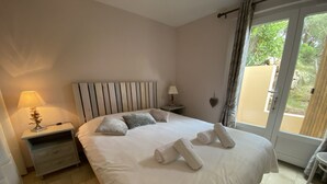 Una cama bien tendida con toallas, una lámpara de noche y una mesita de noche en una habitación con vistas a través de un ventanal.