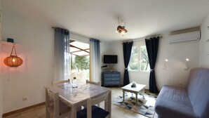Un área de comedor con una mesa y sillas, un sofá, un televisor y un ventanal con cortinas.