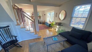 A spacious living room with a staircase, a blue sofa, a coffee table, and a large window.