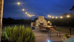 An outdoor patio with a stone fireplace, a dining table, and chairs.