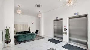 Un hall d’entrée moderne avec un canapé vert, des plantes en pot, un sol en marbre et deux ascenseurs.