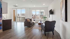 Un salon moderne avec un canapé, un fauteuil et une table basse, de grandes fenêtres et une vue sur la ville.