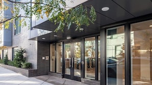 Un bâtiment moderne doté de grandes portes et fenêtres en verre, d’une façade en briques et d’un arbre au premier plan.
