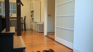 Une pièce avec un plancher en bois, un bureau avec une chaise, une armoire et une paire de pantoufles posées sur le sol.