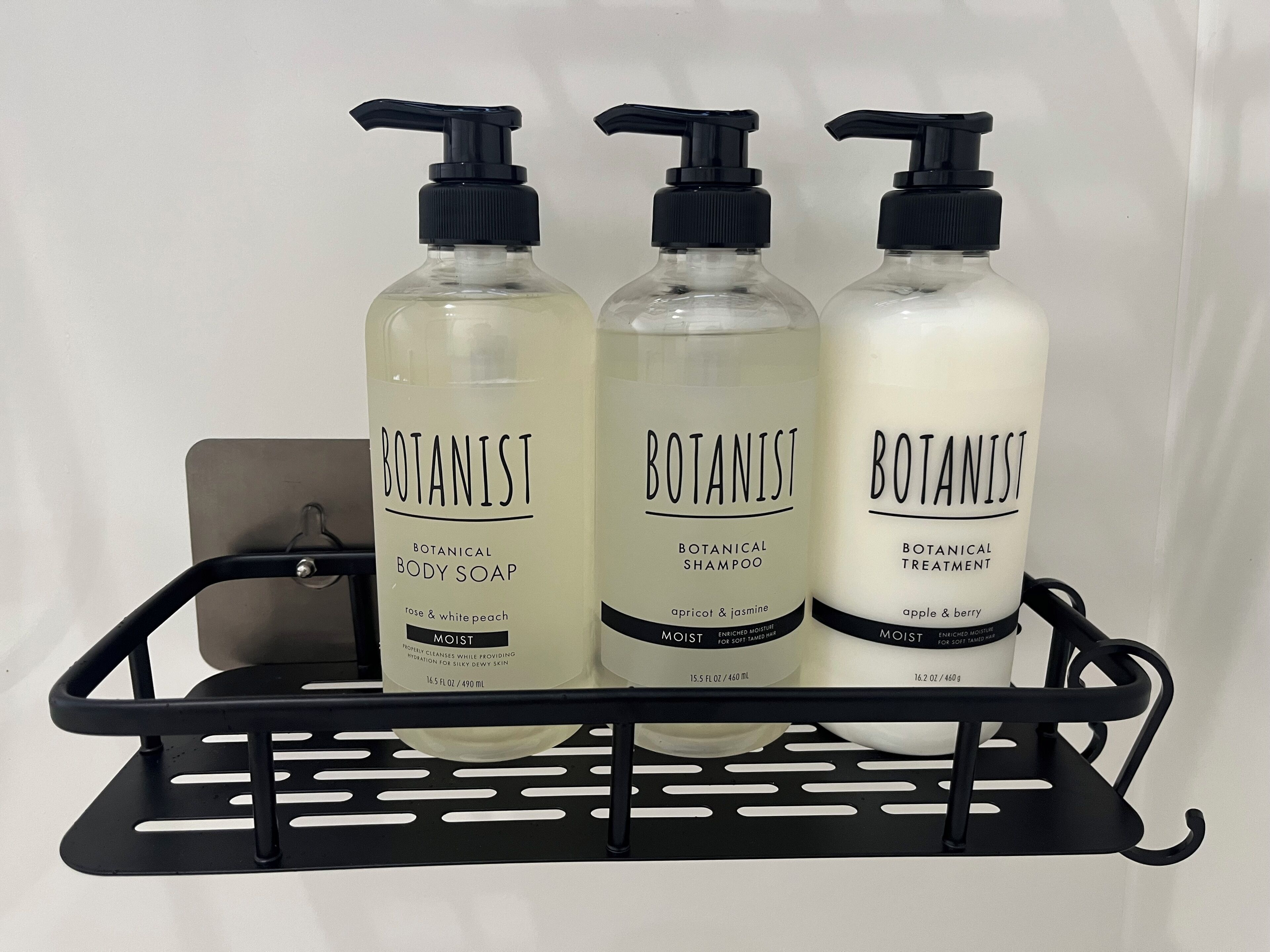 Three bottles of Botanist body soap, shampoo, and treatment on a black metal shelf.