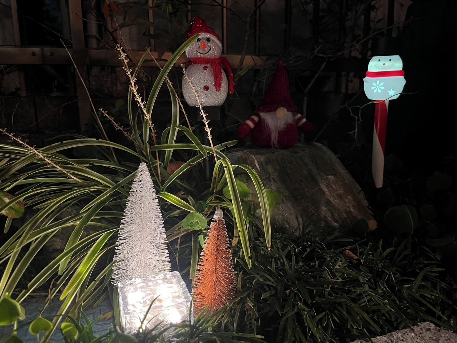 Ein Felsengarten mit verschiedenen Dekorationselementen, darunter eine Schneemannfigur, eine Weihnachtsmannfigur und eine laternenförmige Schneemannleuchte.