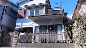 Un immeuble résidentiel à deux étages, doté d’un balcon à l’étage supérieur, d’une entrée sécurisée par un portail et d’un mur en pierre.