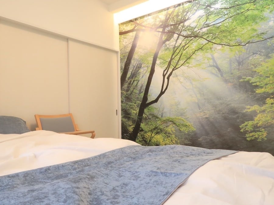 A bedroom with a bed, a chair, and a large forest mural on the wall.