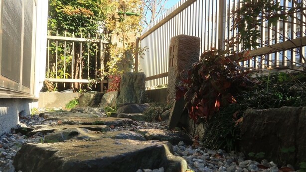 Un chemin de pierre mène à un bâtiment doté d’une grille en métal et d’un pilier en pierre.
