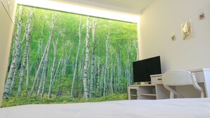 Une chambre avec une grande fenêtre, un lit, un bureau avec un ordinateur et un téléviseur.