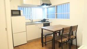 Une cuisine compacte avec des meubles blancs, un four à micro-ondes, une cuisinière et une fenêtre équipée de stores.