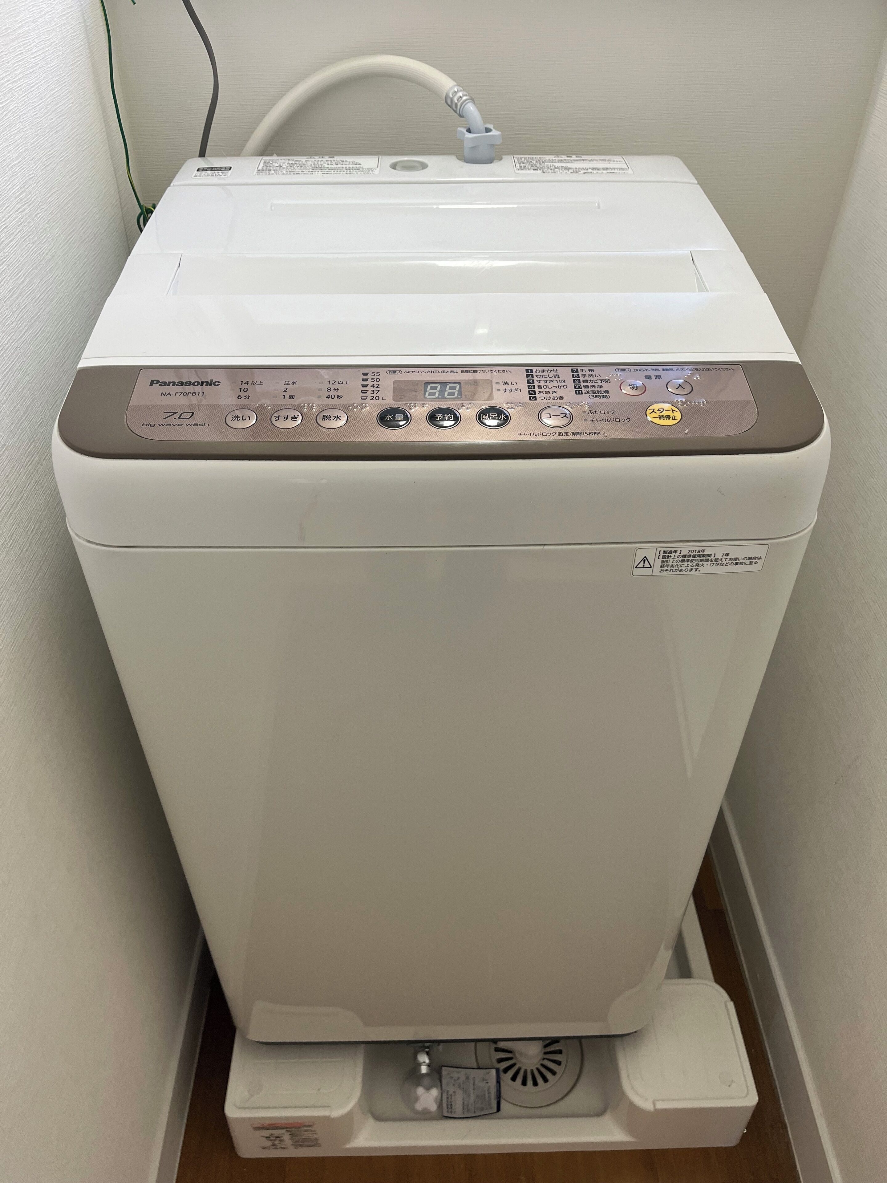 Eine weiße Panasonic Waschmaschine mit Bedienfeld, Zulaufschlauch und Ablaufschlauch.