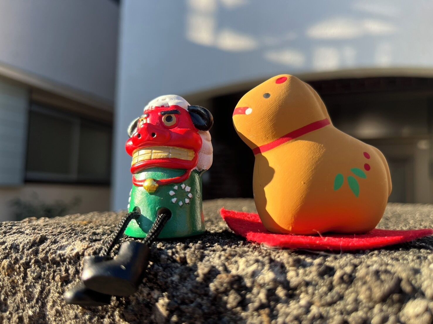 Two ceramic figures on a textured surface with a building in the background.