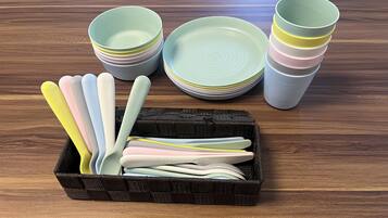 A kitchen with a wooden table displaying a stack of plates and bowls, and a basket containing utensils.