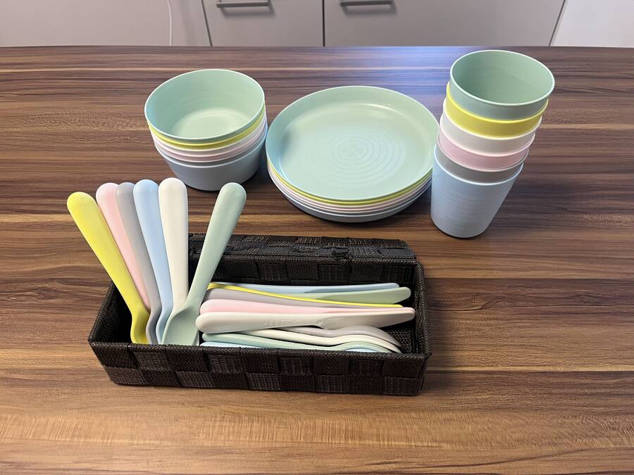 A kitchen with a wooden table displaying a stack of plates and bowls, and a basket containing utensils.