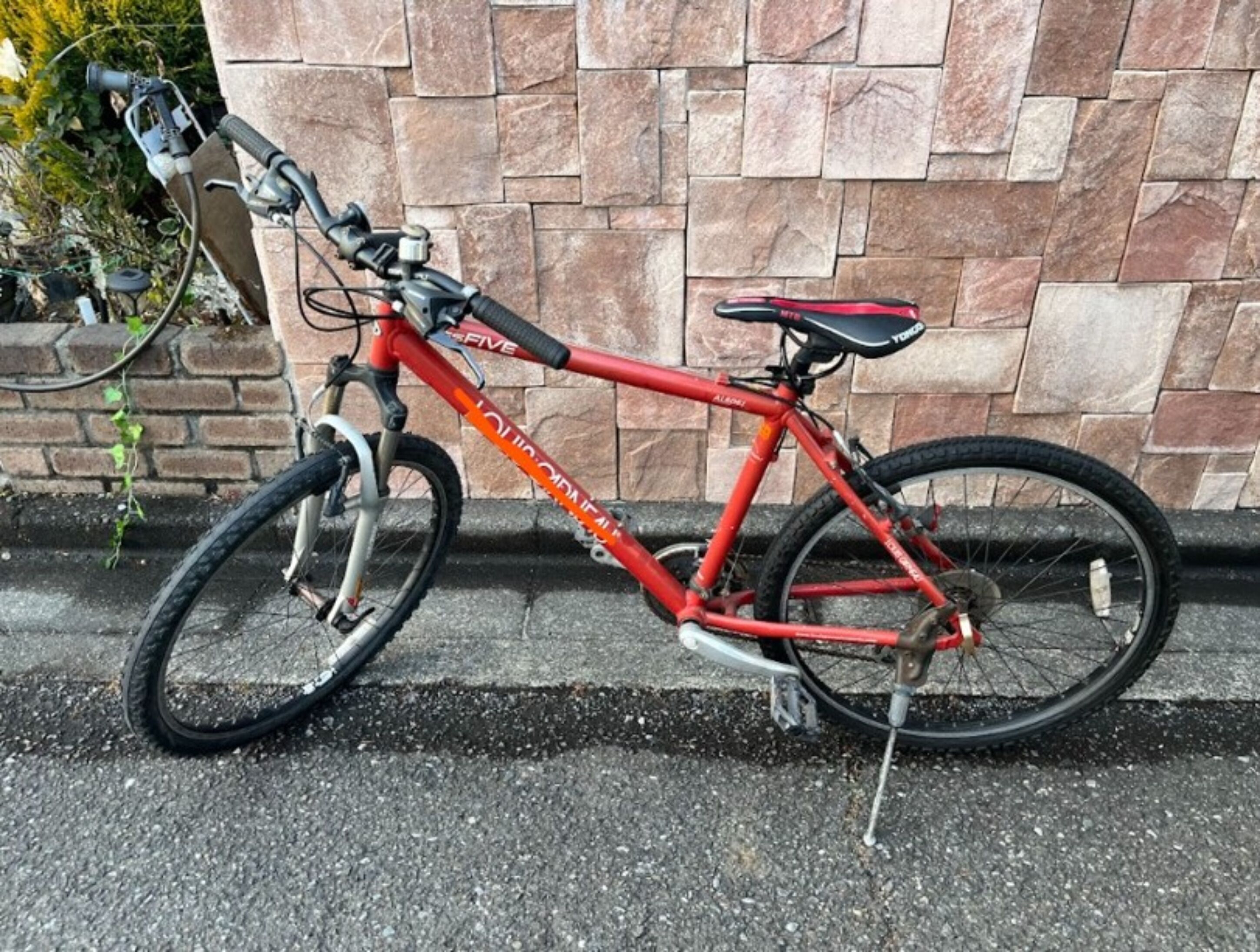 Una bicicleta vermella aparcada davant d'una paret de pedra.