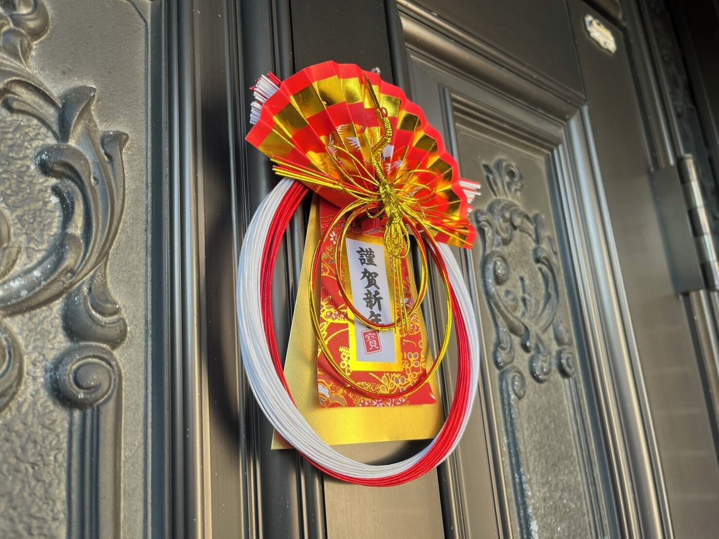 Une décoration traditionnelle chinoise aux couleurs rouge et or, comprenant un éventail et un sceau rouge apposé sur une porte.