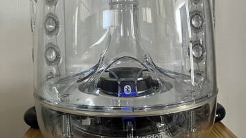 Un oggetto a forma di cupola trasparente con diverse aperture circolari, con la scritta "harman kardon", su una superficie in legno.