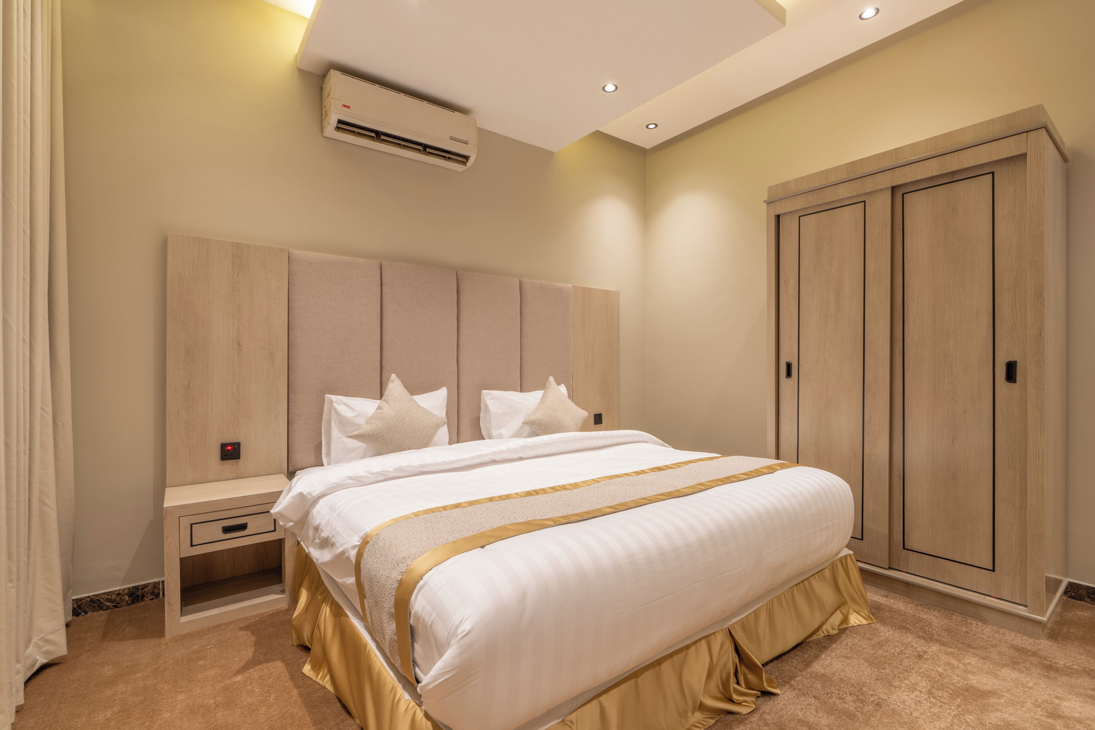 A hotel room with a large bed, a nightstand, a wardrobe, and an air conditioning unit.
