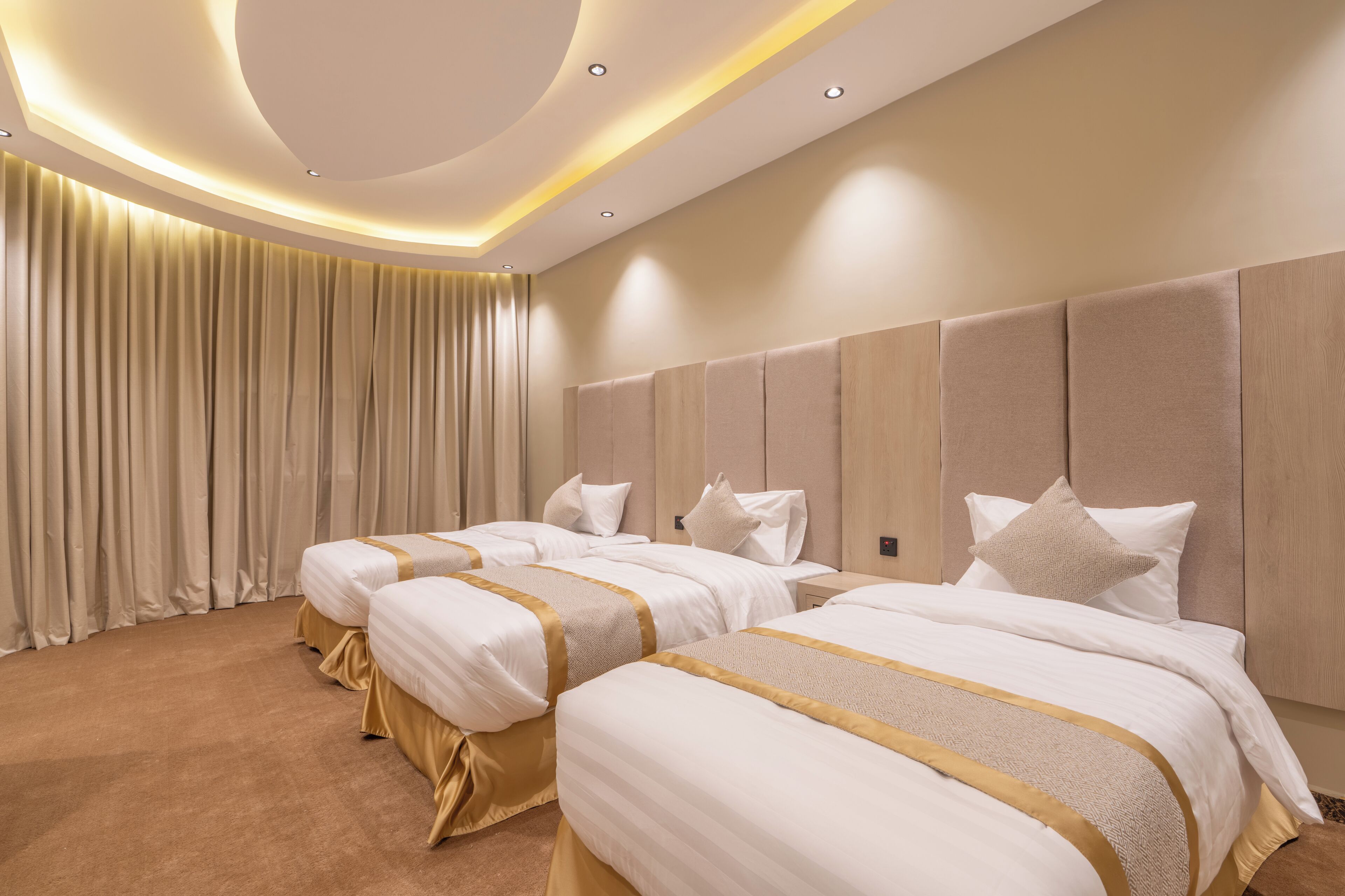 Habitación de hotel con tres camas, un ventanal grande con cortinas y un diseño de techo moderno.