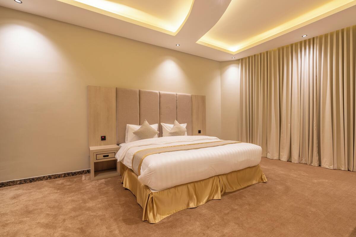 A modern hotel room with a large bed, a nightstand, and a headboard with built-in lighting.