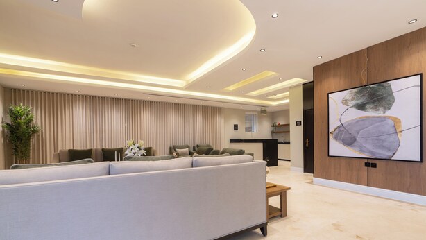 A modern living room with a sectional sofa, a wooden coffee table, and a large abstract painting on the wall. - Deyala Serviced Apartments 4 (Riyadh)