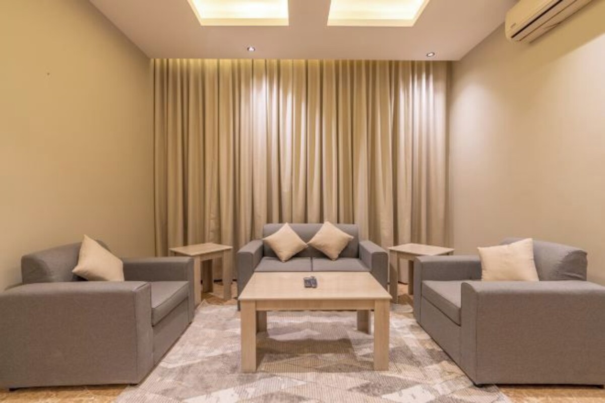 A modern living room with two grey sofas, a central coffee table, and a large window with vertical blinds.
