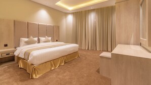 A modern hotel room with a large bed, a wooden headboard, a bedside table, and a built-in bench. - Deyala Serviced Apartments 4 (Riyadh)