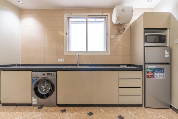 A compact kitchen with a built-in washer, a microwave, and a refrigerator. - Deyala Serviced Apartments 4 (Riyadh)