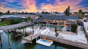 A modern house with a glass-enclosed patio, a pool, and a dock with kayaks. - Waterfront | Dock, Htd Pool, Hot Tub & Game Room (Apollo Beach)