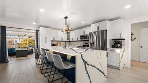 A modern kitchen with white cabinets, a marble island, and a stainless steel refrigerator. - Waterfront | Dock, Htd Pool, Hot Tub & Game Room (Apollo Beach)