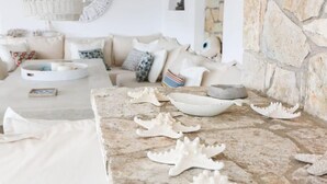 Uma sala de estar acolhedora com uma mesa de pedra, decorações de estrelas-do-mar e um sofá branco com almofadas estampadas.