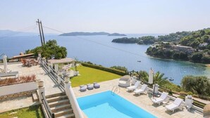 Área da piscina com vista para o mar, mobiliário de exterior e escadaria que dá para um deck.